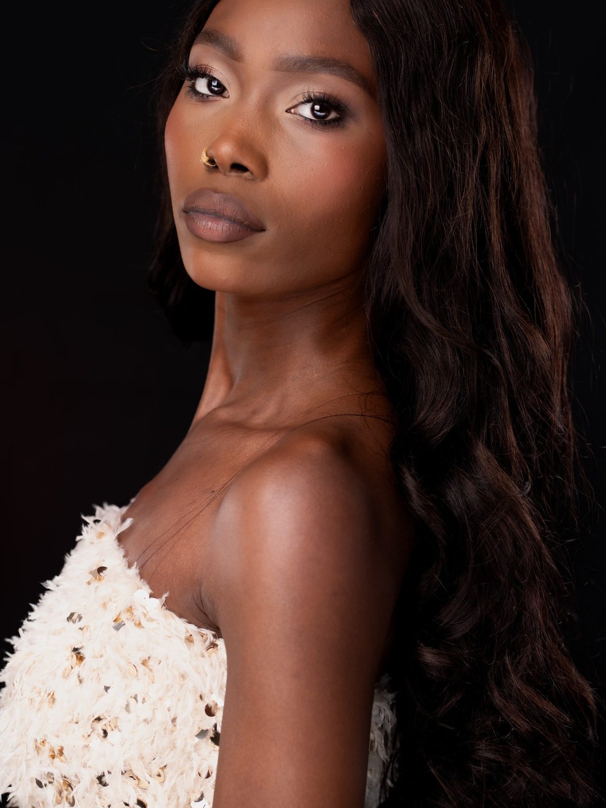 Model Gloria kijkt over haar schouder: soft glam met bronzen ogen, lange donkere krullen, zwarte achtergrond