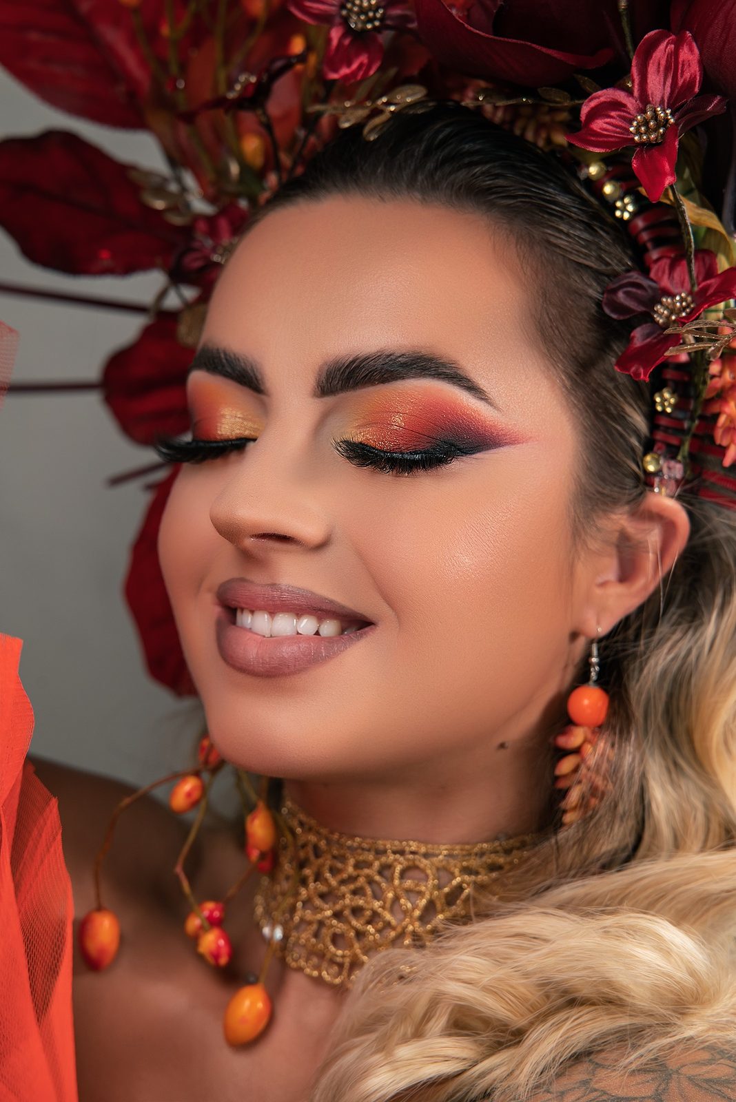 Herfst-editorial: oranje en rode cut crease, een krans van rode bloemen en oranje bessen in het haar