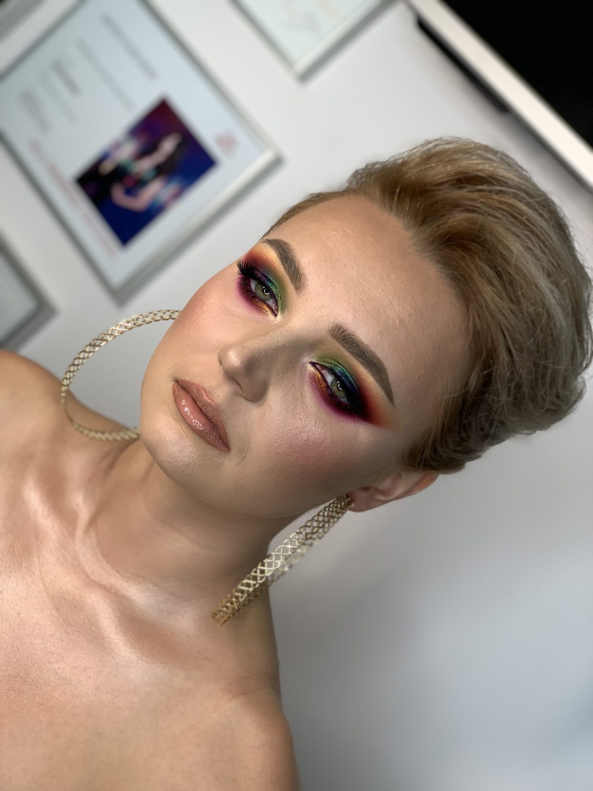 Model met kort opgestoken haar, een kleurrijke cut crease en grote gouden oorbellen